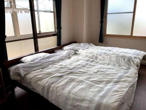 an unmade bed in a bedroom with two windows at Big stone tsukuda / Vacation STAY 5836 in Aomori