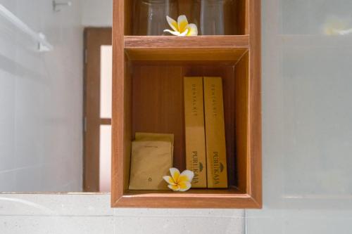 a wooden book shelf with two books and two flowers at Puri Kaja House in Badung