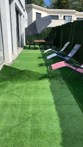 a row of lounge chairs and an umbrella on a lawn at EXCEPTIONNEL Studio VERSAILLES in Le Chesnay