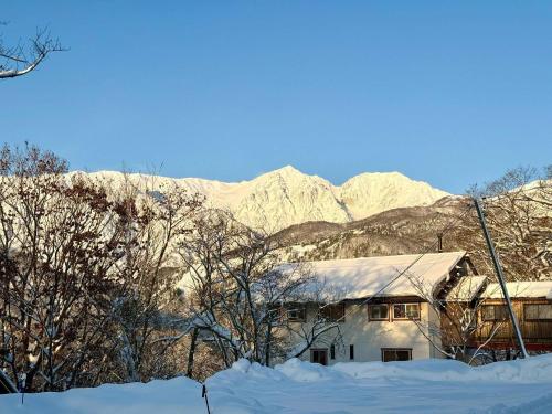 a house covered in snow with mountains in the background at The Nook Hakuba in Hakuba