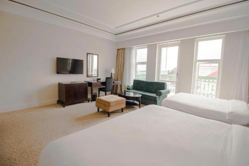 a white hotel room with two beds and a chair at La Sapinette Hotel Dalat in Da Lat