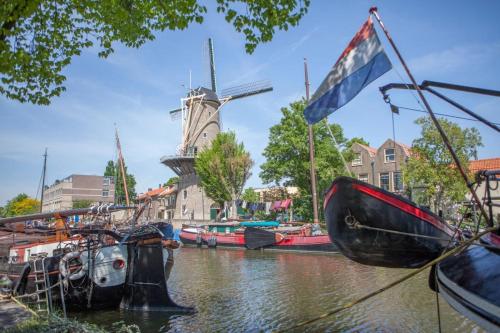 a group of boats in a canal with a windmill at Gouda city center apartment with private garden and 2 bicycles in Gouda