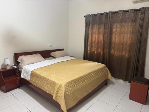 a bedroom with a bed with a yellow blanket and curtains at Christie's Apartment in Accra