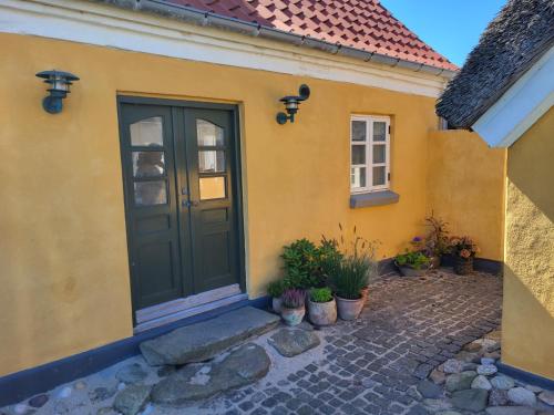 a yellow house with a green door and some plants at Strandhuset in Agger