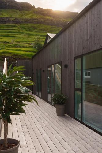 a wooden deck with a house and a plant at Hotel Vík - 3 BR Wellness Townhouses with Sauna, Jacuzzi & Panoramic Views in Haldarsvík