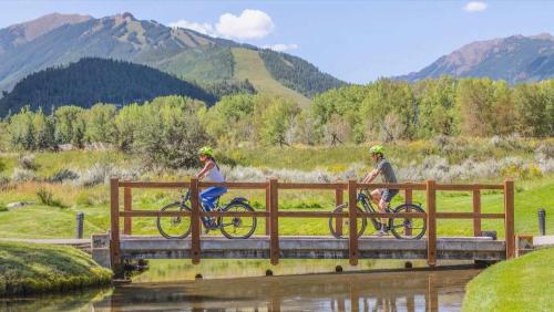 two people riding bikes on a bridge over a river at Renovated 2 BR Aspen Condo Ski-in out in Aspen