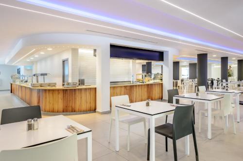 a restaurant with white tables and chairs and a counter at Hotel Vibra s'Estanyol in San Antonio Bay