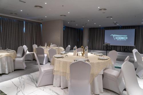 a conference room with tables and white chairs and a screen at VOGO Grand Hotel Formerly Best Western Plus Hotel Dubai Academic City in Dubai