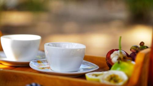two cups and plates on a table with fruit at Jungle Crown Cabin in Sigiriya