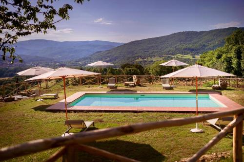 a swimming pool with umbrellas and chairs with mountains in the background at Restored Farmhouse In Tuscan Casentino Hills in Poppi