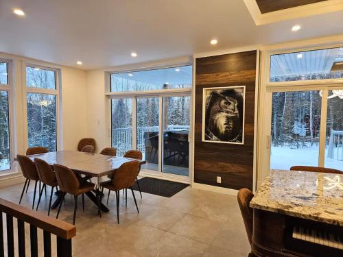 a dining room with a table and chairs and windows at Le repaire du hibou - Piano & Spa in Petite-Rivière-Saint-François