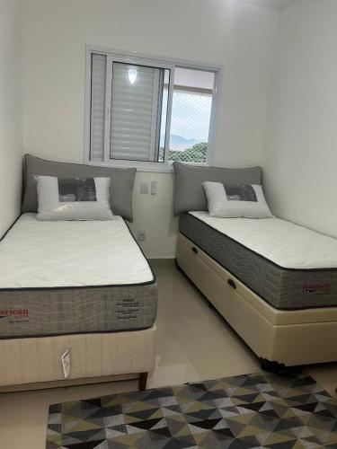 two beds sitting in a room with a window at APARTAMENTO NA PRAIA CENTRO De BERTIOGA in Bertioga