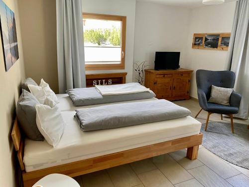 a bedroom with two beds and a chair and a window at Chesa Muntanella in Sils Maria
