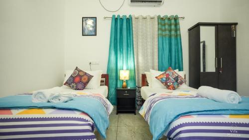 two beds in a room with blue curtains at VILLA MANTRAA in Varkala