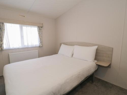 Un dormitorio con una cama blanca y una ventana. en Gold Caravan 316, en Talybont