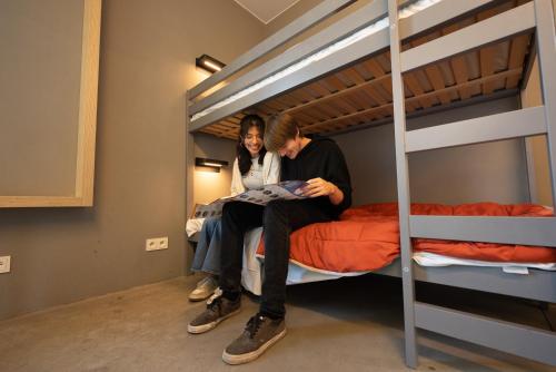 two people sitting on a bunk bed looking at a magazine at Hostel Groeninghe in Kortrijk