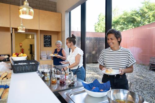 three people standing in a kitchen holding a plate of food at Hostel Groeninghe in Kortrijk