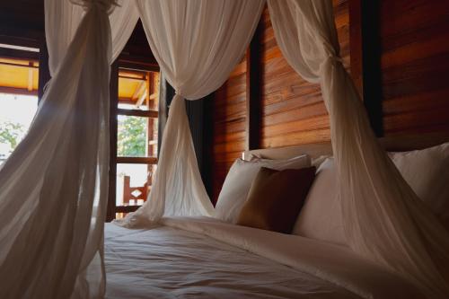 a bedroom with a bed with white drapes and a window at Villa Budalipir - Uluwatu Bali in Uluwatu