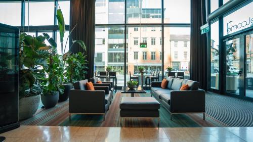 a lobby with couches and plants and windows at The Manchester Deansgate Hotel, by IHG in Manchester