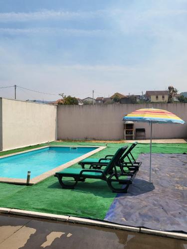 a swimming pool with two picnic tables and an umbrella at Villa Machado Chaves in Vila Nova da Veiga