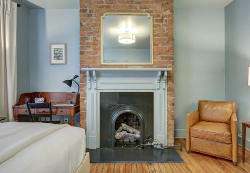 ein Schlafzimmer mit einem Kamin, einem Spiegel und einem Stuhl in der Unterkunft The 200 South St | King Ste 24 in Charlottesville