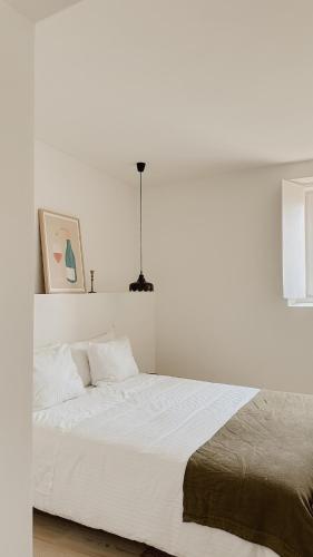 een witte slaapkamer met een groot bed met witte lakens bij Casa do Miradouro in Évora