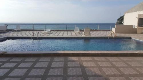 a swimming pool with chairs and the ocean in the background at Departamento Manta in Manta