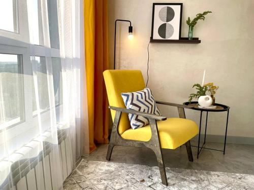 a yellow chair sitting next to a table and a window at Уютные Апартаменты 1 Минута от Станции Метро in Almaty