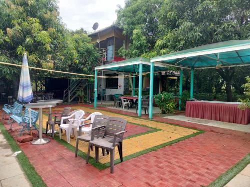 a patio with chairs and tables and a umbrella at Ganraj River Rafting Kolad in Kolād