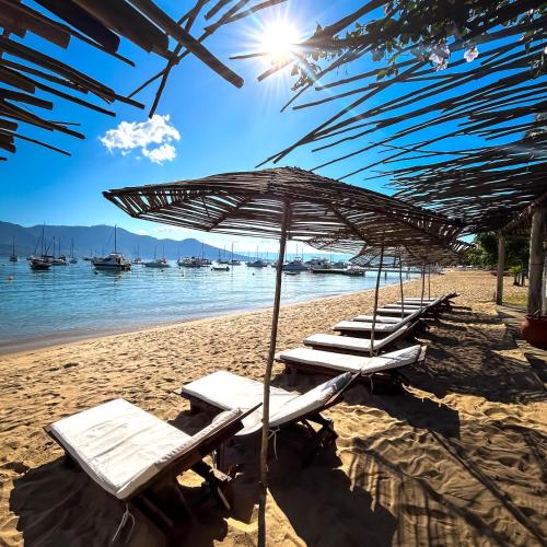 a group of beach chairs and an umbrella on a beach at Hotel Itapemar - Ilhabela in Ilhabela