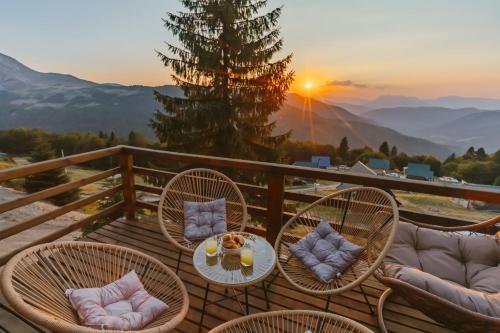a deck with chairs and a table with a sunset in the background at Komovi Luxury House in Andrijevica