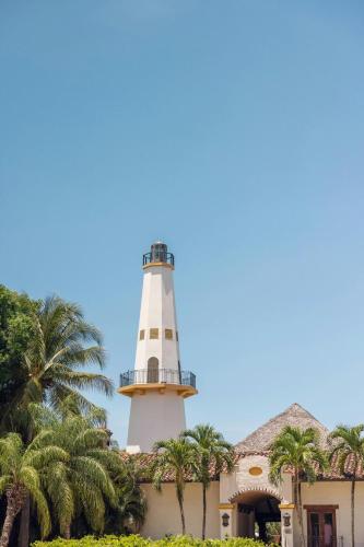 a lighthouse in front of a building with palm trees at The Buenaventura Golf & Beach Resort, Autograph Collection in Playa Blanca