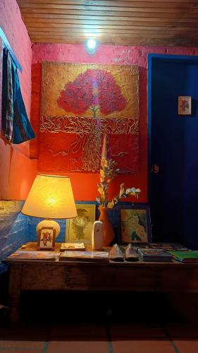 a table with a lamp and a painting of an umbrella at Estancia Hostel in Colonia del Sacramento