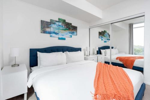 a white bedroom with two beds and a mirror at Stylish Condo with Private Patio in Fortyork in Toronto