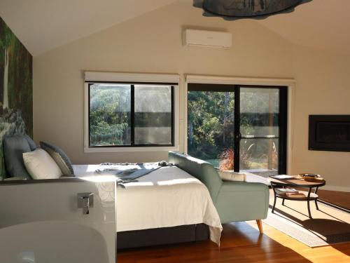 a bedroom with a bed and a chair and windows at Hideaway Falls - Staggys Cottage in Mapleton