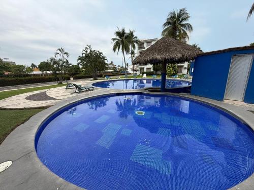 a large blue swimming pool with a building and palm trees at Hermoso y moderno departamento 2Hab, club de paya in Manzanillo