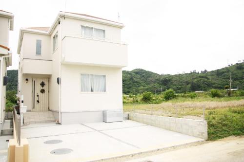a white house with a hill in the background at 海まで徒歩3分の星降るやんばるテラスは1棟貸で古宇利島まで車で10分 in Nago