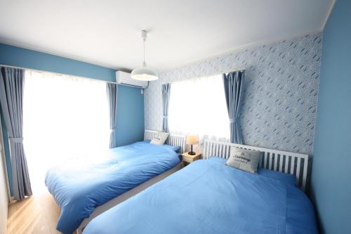 two beds in a bedroom with blue walls and windows at 海まで徒歩3分の星降るやんばるテラスは1棟貸で古宇利島まで車で10分 in Nago
