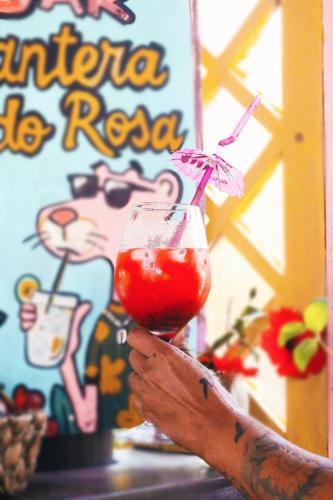 a person holding up a drink in a glass at Hostel Pantera do Rosa in Praia do Rosa
