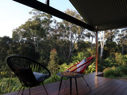 two chairs and a table on a wooden deck at Hideaway Falls - Bunya Cottage in Mapleton