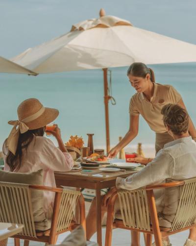 Una mujer sentada en una mesa en la playa con dos personas. en Twinpalms Tented Camp Phuket, en Bang Tao Beach