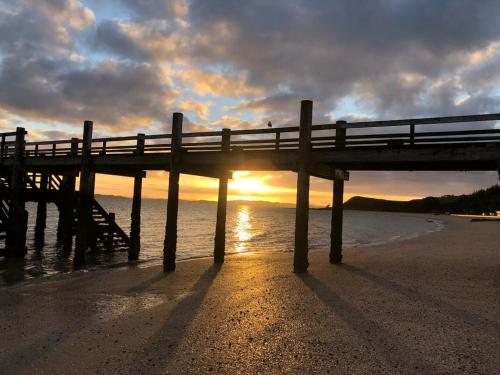 a pier on the beach with the sun setting at Maraetai Beachfront bliss one bedroom apartment in Maraetai