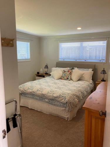 a bedroom with a large bed with two windows at Maraetai Beachfront bliss one bedroom apartment in Maraetai