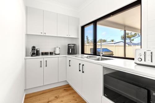 a white kitchen with a sink and a window at Callala Haven - Pet Friendly with Fire Pit in Callala Bay