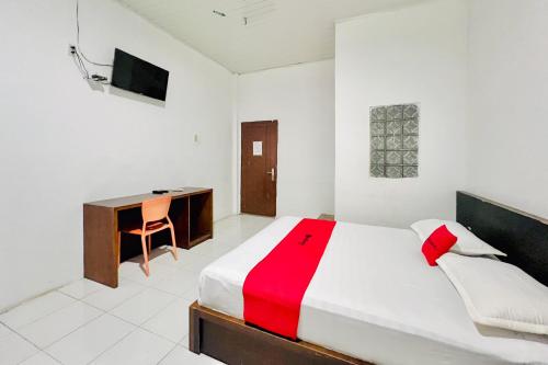 a bedroom with a bed with a desk and a red blanket at RedDoorz Syariah at Hotel Seunia Banda Aceh in Banda Aceh