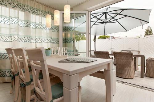 a white dining room table with chairs and an umbrella at Schickes Ferienhaus Ostseeperle, 3 Schlafz., 2 Bäder in Zingst