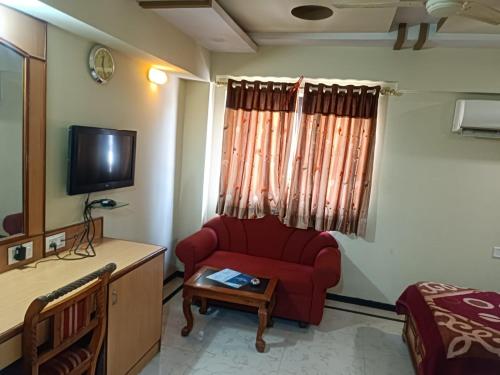 a living room with a red couch and a tv at Hotel Sabar inn in Ahmedabad