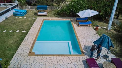 a man standing next to a swimming pool with an umbrella at Villa SAIDIA climatisée avec PISCINE in Diego Suarez
