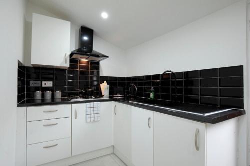 a kitchen with white cabinets and black tiles on the wall at Dixon House, Sleeps 6, Free Parking, Long or Short Stays - by NMB Property in Horwich