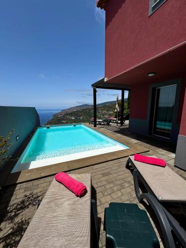 a swimming pool with two chairs and a house at Sunset Dreams - Arco da Calheta in Arco da Calheta
